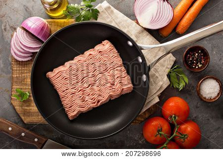Ground turkey in a skillet with raw vegetables ready to be cooked