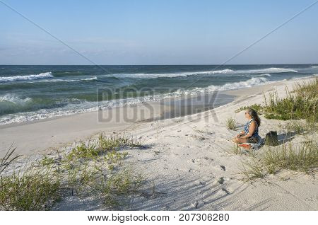 Pretty mature woman sitting in the sand dunes looking out to sea on a windy day in Florida on the Gulf of Mexico.