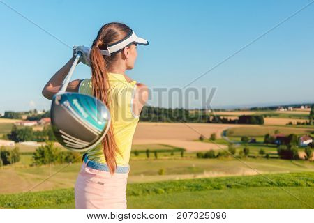 Young woman holding a driver club behind her back during golf swing, at the beginning of a professional match outdoors in a sunny day in the countryside