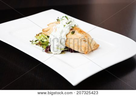 Traditional russian pie - coulibiac. Baked puff pastry filled with smoked salmon, served with sour cream sauce