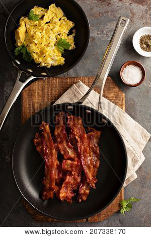 Cooked sizzling hot tasty crispy bacon on a skillet and scrambled eggs ready for breakfast overhead shot