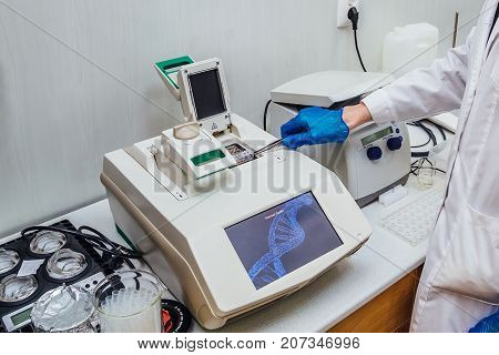 Scientist with gloved hand putting DNA sample into real-time PCR-cycler