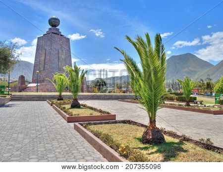View of the Middle of the World monument with a palm tree in the foreground, on a sunny summer morning. Ecuador. Mitad del Mundo.