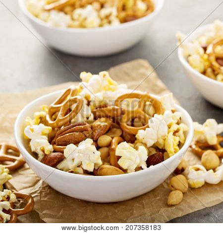 Homemade trail or snack mix with popcorn, pretzels and nuts in white bowls