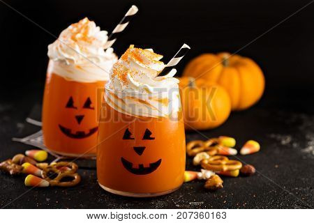 Halloween cold pumpkin cocktail or drink with jack o'lantern face and whipped cream