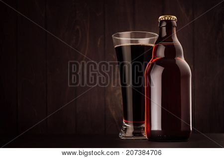 Brown beer bottle belgian steinie and glass pilsner with porter on dark wood board copy space mock up. Template for advertising design branding identity.