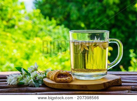 Glass cup of herbal tea jasmine tea and jasmine flowers on an old wooden table with a blurred green natural background. The concept of tea