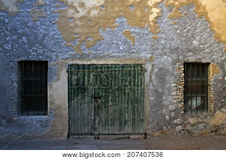 Old wooden gates and two grating windows. Weathered wall of derelict house