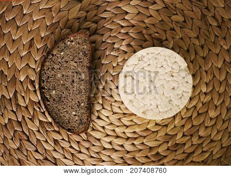 White flat round rice cracker and a piece of rye bread on whicker place mat background.