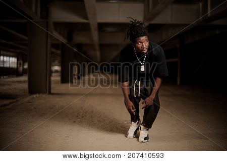 Young afro american man with dreadlocks and dressed in black clothes in the half squat looking aside