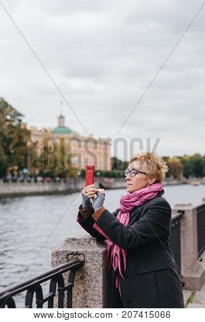 Adult woman standing on waterfront and taking shots with smartphone.