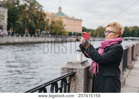 Adult woman standing on waterfront and taking shots with smartphone.