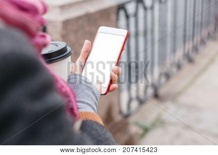 Adult woman in glasses standing with smartphone and coffee on waterfront.