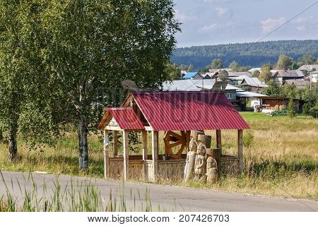 Wooden well and statues of the three Russian heroes in the old believer village Visim.  Sverdlovsk region, Russia.