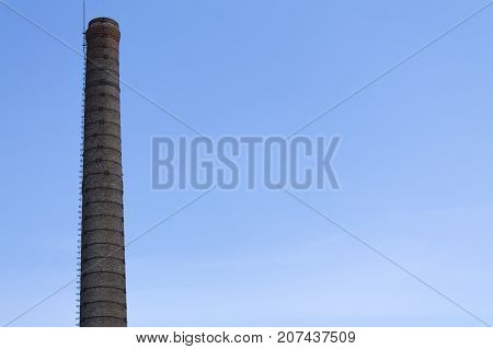 A chimney of an old factory made of bricks against a blue sky.