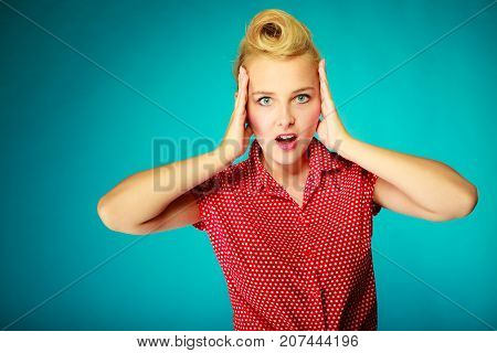 Shocking amazed astonished gestures concept. Shocked lovely pin up young girl holding head with hands. Studio shot on blue background