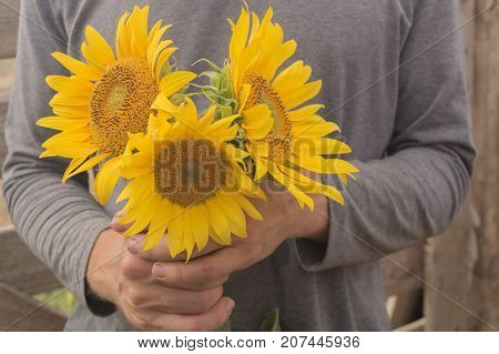 Man in grey turtleneck holds three sunflowers in his arms