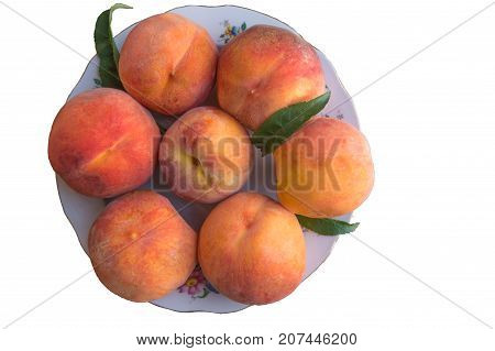 Seven ripe peaches with green leaves in a ceramic plate isolated on white background
