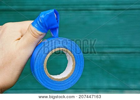 blue sticky tape on fingers of a hand on a green background