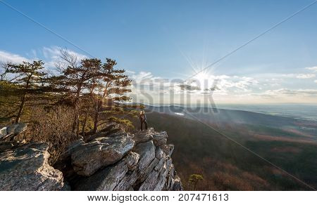 Female hiker standing in the wind at the edge of a rocky cliff on the summit of an Appalachian mountain enjoying the sunset and vista