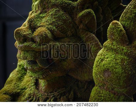 Balinese Carved Stone Statue of Rakasa covered with green moss. at Hindu Temple.
