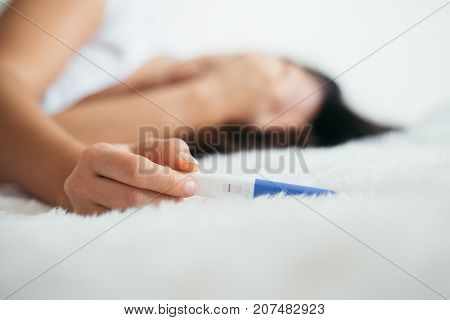 Upset woman lie sad in white bed with negative pregnancy test
