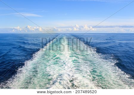Trail on water surface behind the ferry with clouds and sky in the background