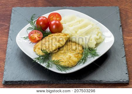 Two juicy fried meat patties on a white plate with cherry tomatoes and mashed potatoes.