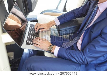 Close-up of a young businessman who uses a laptop to work in the backseat of a car.