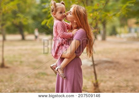 Mother and daughter walking in the park holding a beautiful daughter in her arms.