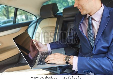 Close-up of a young businessman who uses a laptop to work in the backseat of a car.