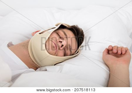 Young Handsome Man Sleeping With Anti Snoring Chin Strap On Head At Home