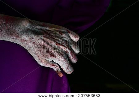 closeup of the scary hand of an undead man drawing a purple stage curtain, with a blank black background in the background