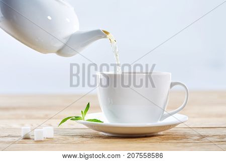 Pouring green tea from white ceramic teapot into a matching tea cup