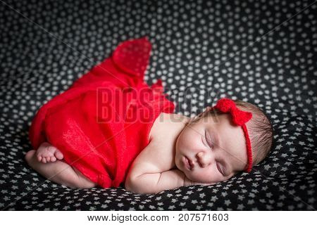 Sleeping pretty newborn in red dress and a small ribbon on his head.