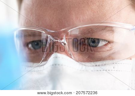 A portrait of a young surgeon chemist's doctor looks at a container with a blue liquid and a mask is fought with viruses and a vaccine for vaccines against diseases
