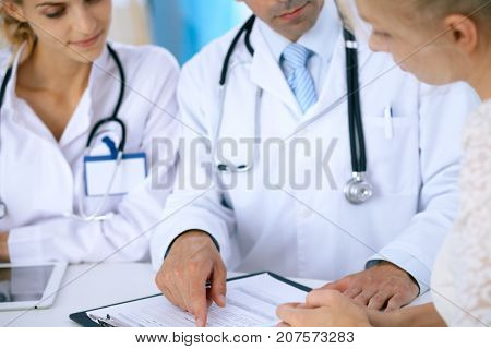 Doctor and  patient talking while sitting at the desk in office. Physician pointing into medical history form. Medicine and health care concept.