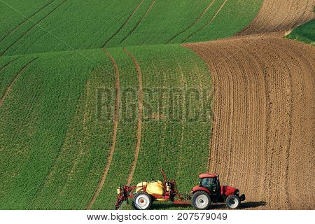 Modern Red Tractor Plowing And Spraying On Field. Small Tractor Working On A Colorful Spring Field.Agriculture Tractor Creating Abstract Brown Background Texture.Rural Scenic Landscape.Czech Republic