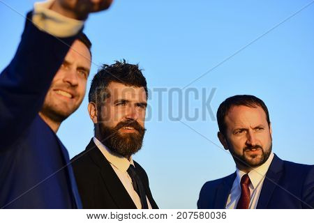 Businessmen with smiling faces in formal suits and ties on blue sky background. Business confidence and teamwork concept. Company leaders show worksite and new goals. Executives take a walk outside