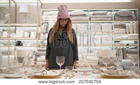 MINSK, BELARUS - OCTOBER 10, 2017. Inside Zara Home retail store in Minsk.  A young hipster female in fashion glasses chooses dishes in the store. Shopping