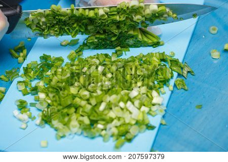 Hands of cheaf cutting a green onion. A chopped green onions on a wooden board with a knife.