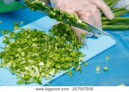 Hands of cheaf cutting a green onion. A chopped green onions on a wooden board with a knife.