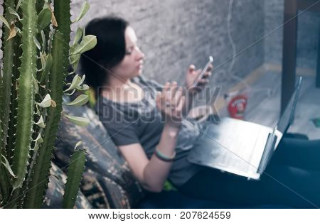 the cactus in the foreground, a young brunette girl in t-shirt and jeans, selective focus, lying on the bed in my bedroom to play video games on your smartphone, write letters, open the laptop