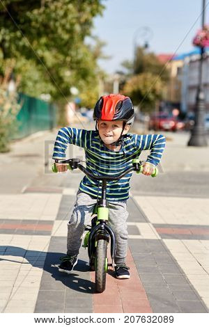 Boy in helmet standing with bike at autumn park. Happy active child