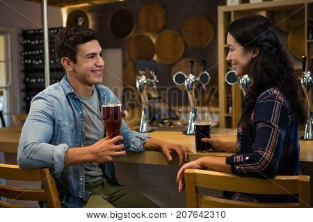 Young friends enjoying drinks while sitting at counter on chair in bar