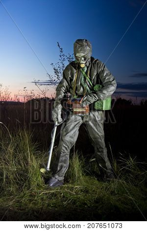 Radiation supervisor in protective clothing and gas mask with geiger counter checks the level of radiation in the radioactive zone