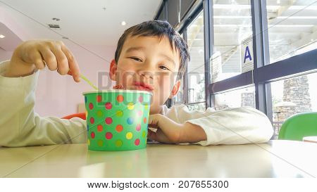 Cute Young Chinese and Caucasian Boy Enjoying Eating His Frozen Yogurt.