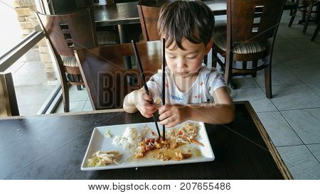 Cute Young Chinese and Caucasian Boy Learning To Use Chopsticks At Restaurant.