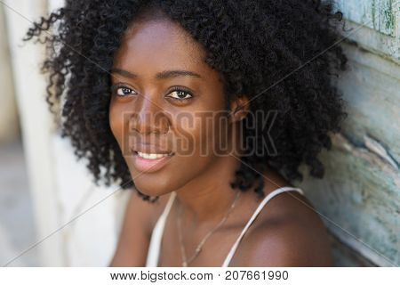 Closeup portrait of smiling young attractive African American woman looking at camera with old wooden wall in background