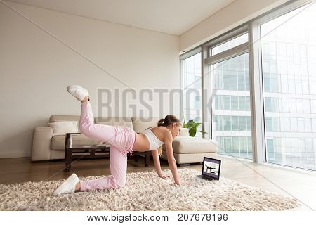 Young sporty woman working out at home, teenager doing fitness exercises on living room floor for buttocks legs shaping using online personal training program, doing yoga pilates indoors, copy space